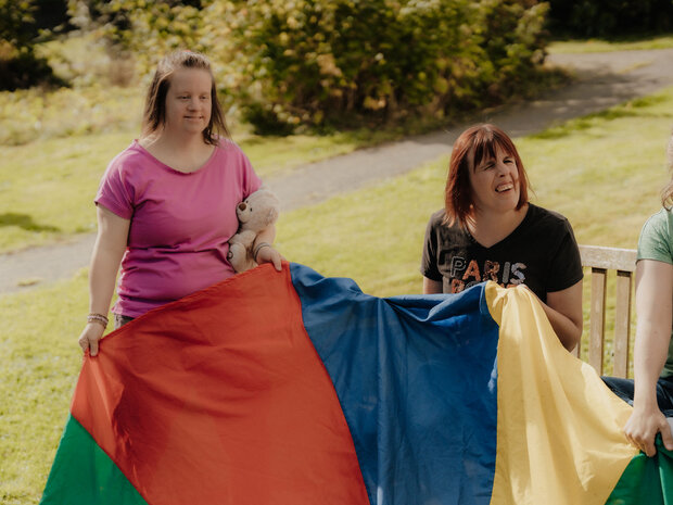 Menschen spielen mit einem bunten Tuh im Garten