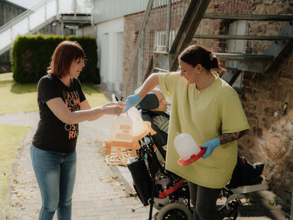 Zwei Frauen bei der Befüllung von Hühner-Futter-Spender-Boxen