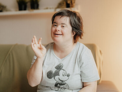 Eine Bewohnerin sitzt auf der Couch und winkt glücklich in die Kamera