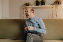 Bewohner des Wohnhauses bei Noh Bieneen sitzt lachend auf dem Sofa